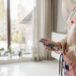 Person injecting medication into abdomen at home, wearing casual clothing, next to large window with plants